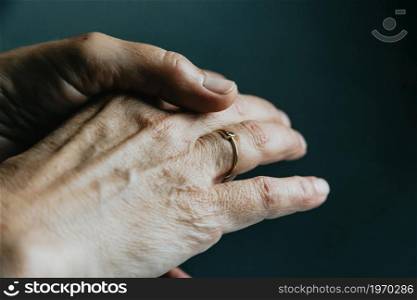 A pair of old hands showing a jewelry ring on the finger over a dark background