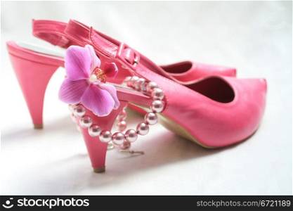 A pair of pink leather ladies shoes, a pink orchid and a pearl necklace