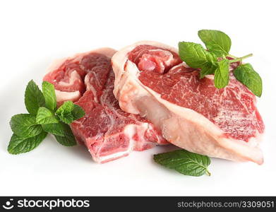 A pair of raw lamb chops, with mint and a clove of garlic, on a white plate