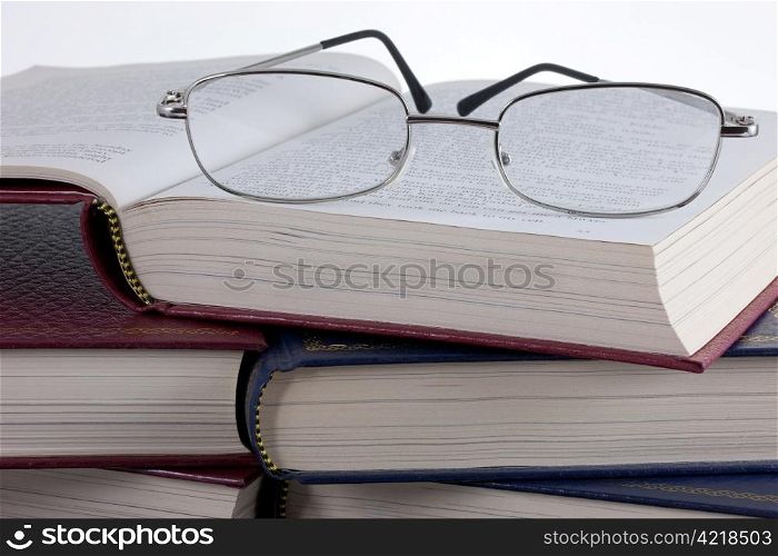 A pair of reading glasses on a pile of old, leather bound books