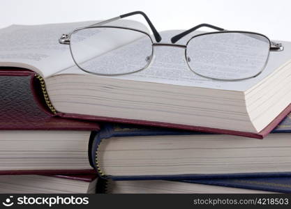 A pair of reading glasses on a pile of old, leather bound books