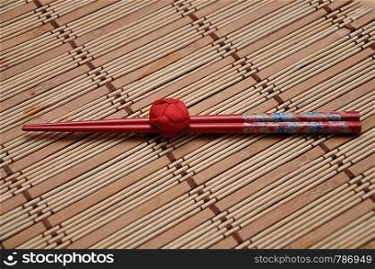 A pair of red chopsticks tied together on a bamboo place mat