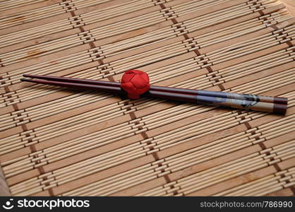 A pair of red chopsticks tied together on a bamboo place mat