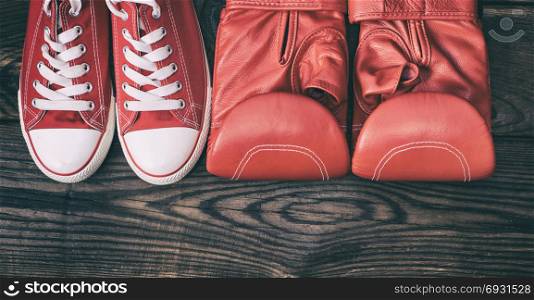 a pair of red sneakers and red leather boxing gloves on a brown wooden background, top view