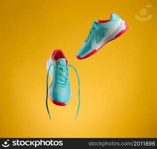 a pair of textile blue sneakers with laces levitate on a yellow background. Shoes for sports, jogging