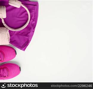 a pair of textile purple sports sneakers, wireless headphones, a towel and a bottle of water on a white background. Sportswear, copy space
