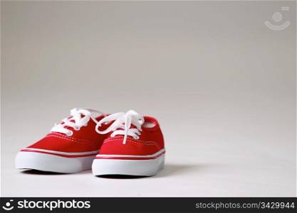 a pair red children shoes. a pair of red shoes with white laces on a clean creme / white background isolated.