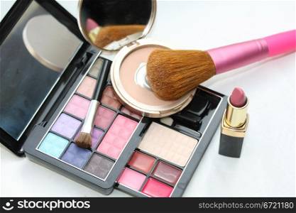A palet with different shades of eye shadow, a compact powder, pink lipstick and a brush