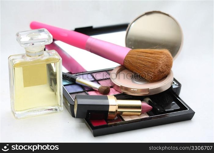 A palet with different shades of eye shadow, perfume bottle, a compact powder, pink lipstick and a brush