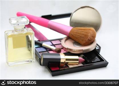 A palet with different shades of eye shadow, perfume bottle, a compact powder, pink lipstick and a brush