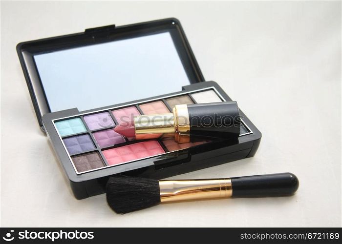 A palet with different shades of eye shadow, pink lipstick and a brush
