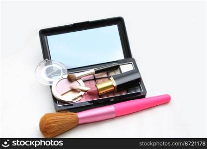 A palet with different shades of eye shadow, pink lipstick and a brush