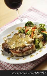 A pan fried pork chop served with coconut sauce and vegetables with a glass of red wine