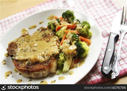 A pan fried pork chop with coconut sauce and vegetables on the side