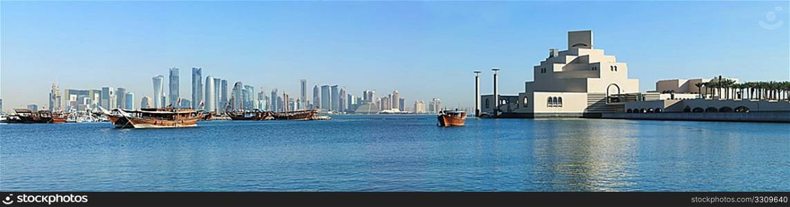 A panoramic view of the skyline of Doha, seen from the corniche with moored dhows and the Museum of Islamic art in the foreground