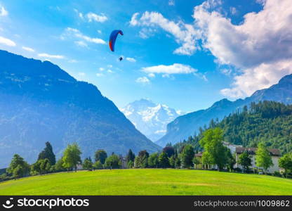A paraglider flying at Hohematte Park in the center of Interlaken, important tourist center in the Bernese Highlands, Switzerland. The Jungfrau is visible in the background. Paraglider in Interlaken, Switzerland
