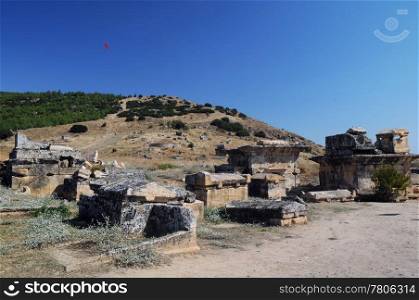 A paraglider is flying over ancient town of Hierapolis in Turkey in the background of the blue sky.