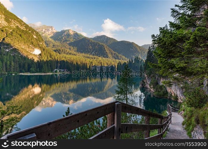 A path with a wooden fence climbs steeply beside the Braies lake, mountain landscape in South Tyrol