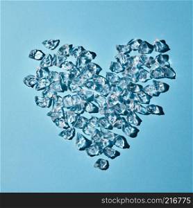 A pattern of transparent ice cubes in the shape of a heart on a blue paper background with copy space. As a background for a postcard. Flat lay. Heart of cold ice cubes on a blue paper background. Layout for your ideas. Flat lay