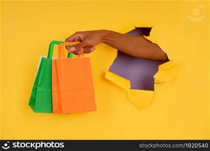 A person holding colourful bags through a hole in paper wall. Shop concept.