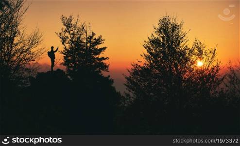 A person in silhouette photographs the sunset on the hillside