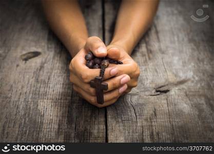 A person praying holding a rosary in the hands on wood background.