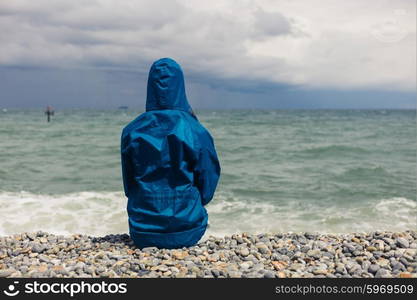 A person wearing a blue jacket is sitting on the beach on a windy day