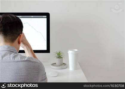 A person working with serious expression at office with personal computer screen that have a coffee and tillandsia air plant with space for text on white wall for working and office concept.
