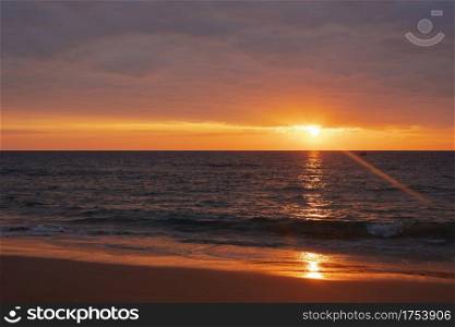 A photo of a sunset landscape where the sea is reflected in the orange light and the blue water is refreshing. At Bang Tao Beach, Phuket Province, Thailand. Concept about travel, nature. No people.