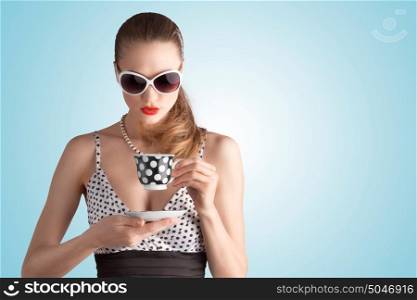 A photo of pin-up girl in spotted dress and sunglasses holding a cup.