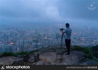 A photographer hiking and looking at city on rock, mountain hill in Hong Kong downtown in adventure concept during travel trip, vacation, or holidays. Skyscraper and high-rise buildings view.