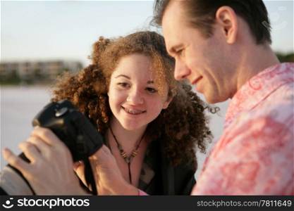 A photographer showing his photos to a friend. Focus is on the girl and her reaction. Warm late afternoon sun.