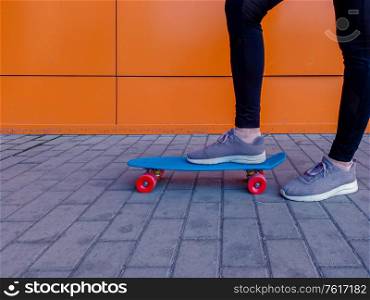 A picture of a girl who put her foot in sneakers on a skateboard against bright orange wall. A picture of a girl who put her foot in sneakers on a skateboard.
