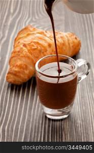 A picture of crunchy croissant and cup of hot chocolate pouring from pot.