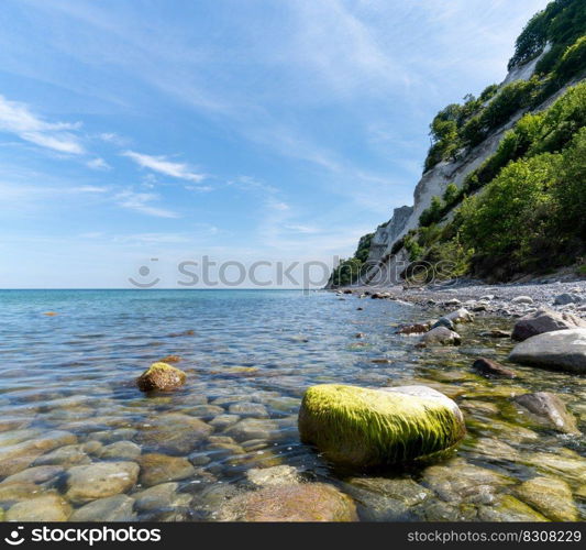 A picturesque ocean and coastline with calm clear water and steep white chalkstone cliffs under a blue sky with white cumulus clouds