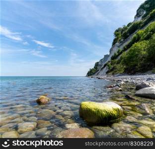 A picturesque ocean and coastline with calm clear water and steep white chalkstone cliffs under a blue sky with white cumulus clouds