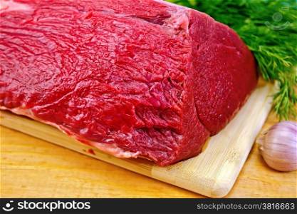 A piece of beef, garlic, dill on a wooden boards background