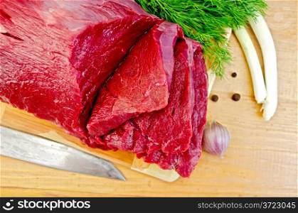 A piece of beef, garlic, peas pepper, dill, chives, knife on a wooden board