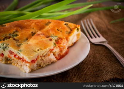 A piece of cake with chicken, herbs and tomatoes on a plate. Homemade delicious food for diet.. Homemade pie with chicken, herbs and tomatoes on a plate.
