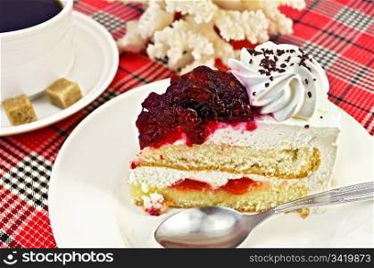 A piece of cake with white cream and red jelly on the plate, a white porcelain cup of coffee with two lumps of sugar, white coral on a background of red plaid fabric