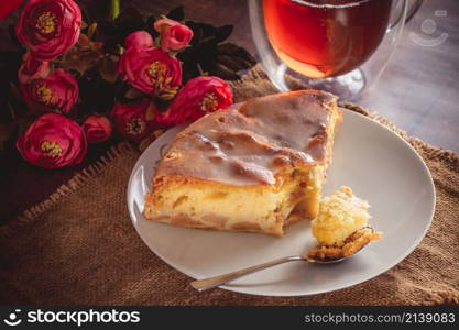 A piece of delicious apple strudel and a spoon on a plate. Amber tea in a transparent cup on a brown background. A piece of apple pie on a white plate on a background of pink flowers