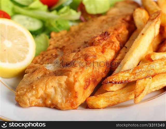 A piece of fish in batter served with french fried potato chips, lemon and a lettuce, rocket, cucumber and tomato salad.