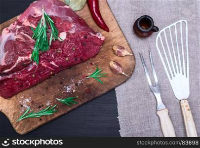 a piece of fresh beef on a wooden board, next to a kitchen plug and a spatula, a top view