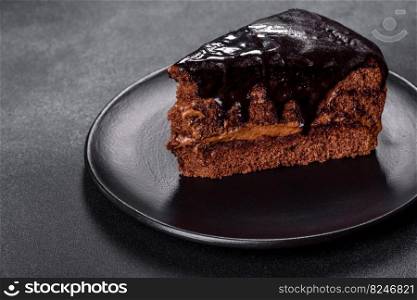 A piece of fresh delicious cake with nuts and chocolate on a black plate against a dark blue background. Desserts and sweets to the dinner table. A piece of fresh delicious cake with nuts and chocolate on a black plate