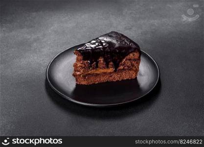 A piece of fresh delicious cake with nuts and chocolate on a black plate against a dark blue background. Desserts and sweets to the dinner table. A piece of fresh delicious cake with nuts and chocolate on a black plate