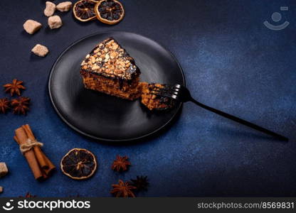 A piece of fresh delicious cake with nuts and chocolate on a black plate against a dark blue background. Desserts and sweets to the dinner table. A piece of fresh delicious cake with nuts and chocolate on a black plate against a dark blue background