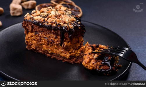 A piece of fresh delicious cake with nuts and chocolate on a black plate against a dark blue background. Desserts and sweets to the dinner table. A piece of fresh delicious cake with nuts and chocolate on a black plate against a dark blue background