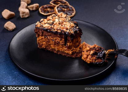 A piece of fresh delicious cake with nuts and chocolate on a black plate against a dark blue background. Desserts and sweets to the dinner table. A piece of fresh delicious cake with nuts and chocolate on a black plate against a dark blue background