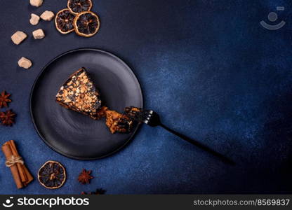 A piece of fresh delicious cake with nuts and chocolate on a black plate against a dark blue background. Desserts and sweets to the dinner table. A piece of fresh delicious cake with nuts and chocolate on a black plate against a dark blue background