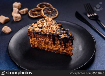 A piece of fresh delicious cake with nuts and chocolate on a black plate against a dark blue background. Desserts and sweets to the dinner table. A piece of fresh delicious cake with nuts and chocolate on a black plate against a dark blue background